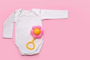 bodysuit for a newborn with a rattle on a pink background with copyspace photo