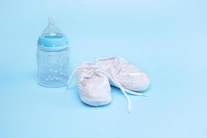 botines para un recién nacido y una botella de fórmula sobre un fondo azul foto