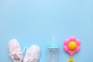 baby booties, formula bottle and rattle on blue background with copy space photo