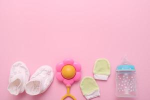 accesorios para un recién nacido: botines, un sonajero, un guante, una botella para mezclar sobre un fondo rosa con espacio para copiar foto