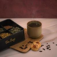 una taza de té junto a una caja con hojas de té y galletas en una mesa foto