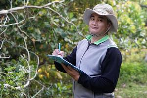 un apuesto botánico asiático está en el bosque para estudiar plantas botánicas, sostiene un portapapeles. concepto, encuesta, investigación de plantas botánicas. conservación de los bosques y el medio ambiente. foto