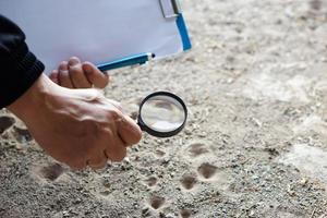 Closeup hand holds magnifying glass to explore tiny insects in holes on ground. Concept, examine, explore, research nature or biological organisms. Study about insects behavior. Science tool. photo