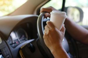 Closeup hand hold paper cup of coffee to drink in car. Concept, baverge for refreshing or helping to awake from asleep during driving that can cause car accident. photo