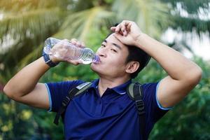 Handsome Asian man holds bottle of drinking water to drink outdoors, Concept  Drinking water for health, Healthy lifestyle.Quenching thirst, reduce fatigue, refresh body. photo