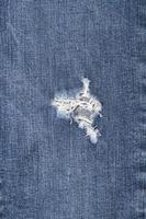 vertical image - Hole and Threads on Denim Jeans. Ripped Destroyed Torn Blue jeans background. Close up blue jean texture photo