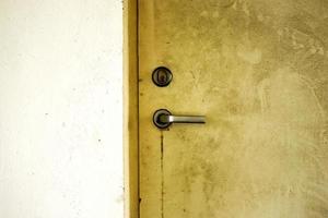 Yellow old weathered dirty door in light concrete wall with a metal handle and a keyhole photo