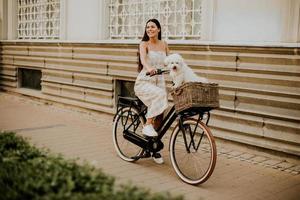 Young woman with white bichon frise dog in the basket of electric bike photo