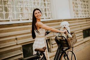 Young woman with white bichon frise dog in the basket of electric bike photo