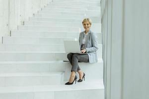 Businesswoman using laptop computer on modern office stairs photo