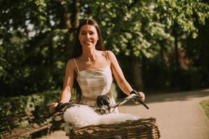 mujer joven con perro bichon frise blanco en la cesta de la bicicleta eléctrica foto