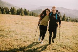 Smiling couple walking with backpacks over green hills photo