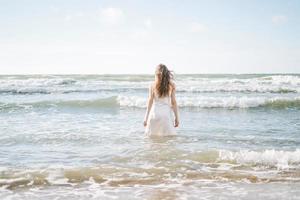 Young blonde beautiful woman with long hair in white dress enjoying life on sea beach photo