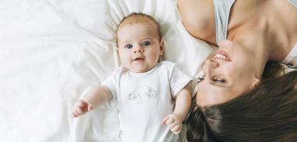 joven madre divirtiéndose con una linda niña en la cama con sábanas blancas, tonos naturales, pancarta foto