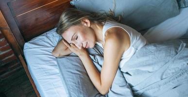 mujer adulta joven con cabello largo rubio durmiendo en la cama en la habitación de loft en el hogar foto