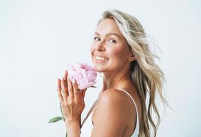 Beauty portrait of blonde hair smiling young woman with pink peony in hand isolated on white background photo