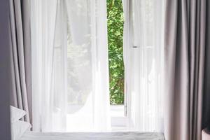 White tulle curtains on the window with green trees on background at home photo