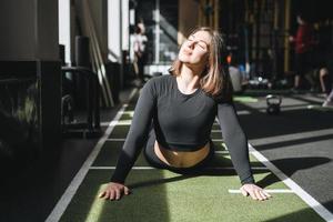 joven morena haciendo pilates de estiramiento, practica yoga en la alfombra en el gimnasio del club de fitness foto