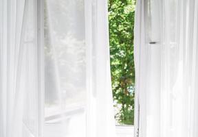 White tulle curtains on the window with view of green trees on background photo