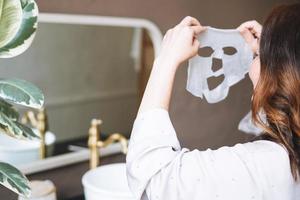 Adult brunette woman with sheet mask on her face in the bathroom at home photo