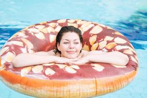 Happy young woman plus size body positive in inflatable doughnut circle swimming in the pool, summer vacations photo