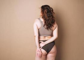 joven mujer atractiva de talla grande en ropa interior de fondo beige, amor corporal foto