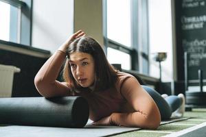 Young brunette woman doing stretching pilates on massage roll in fitness club gym photo