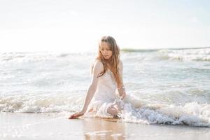 joven mujer rubia hermosa con el pelo largo en vestido blanco disfrutando de la vida en la playa del mar foto