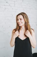 retrato de belleza de moda de mujer joven feliz con el pelo largo en la noche elegante vestido negro en interior blanco foto