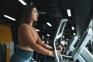 Young brunette woman training for cardio equipment at fitness club gym photo