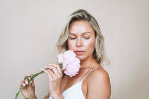 Beauty portrait of blonde hair smiling young woman with pink peony in hand isolated on white background photo