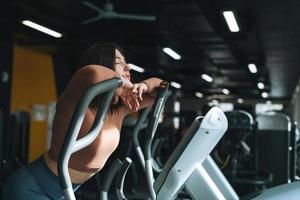 Young tired woman training for cardio equipment at the fitness gym photo