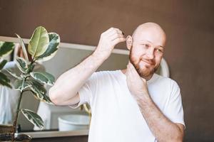 Adult handsome man with pipette with beard oil in bathroom at home photo