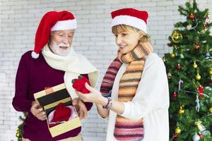 Happy senior caucasian couple wearing Santa hat are celebrating Christmas together and exchanging present in happiness photo