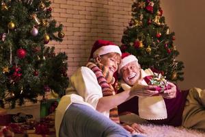 Senior caucasian couple celebrating Christmas together in happiness and excitement at home with red Santa hat and christmas tree photo