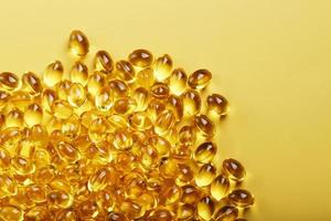 Heap of transparent fish oil capsules on yellow background with free space photo