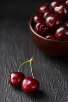 Ripe and juicy cherry berries on a black textural background in a brown cup, with water drops. Top view, close-up. photo