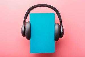 Headphones are worn on a book in a blue hardcover on a pink background, top view. photo
