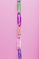 Multicolored paper clips are attached in a row on a pink background photo