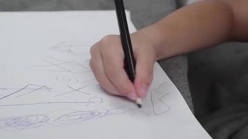 mão de criança segurando um lápis desenhando em papel branco. de uma forma divertida video