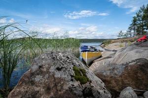 Precioso paisaje. canoa estacionada en la orilla arenosa del lago, con grandes piedras, en un día de verano. estilo de vida. foto