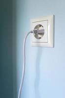 Plug with cable cord connected to the socket, on a blue wall. photo