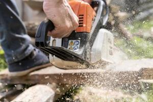 Male hands sawing old boards for firewood with a professional chainsaw, in a village yard. Winter preparation concept. Lifestyle. photo