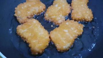 The process of frying the nuggets in a pan with not too much oil. The color of the nuggets is brownish gold, indicating that the nuggets are cooked. video