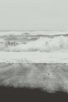 espuma del océano en la foto monocromática del paisaje de la arena negra
