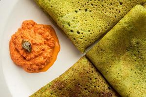 Palak dosa made using mixing spinach or keerai in batter, served with red chutney photo