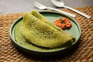 Palak dosa made using mixing spinach or keerai in batter, served with red chutney photo