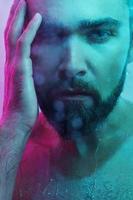 Portrait of handsome young man captured through wet glass in colorful light photo