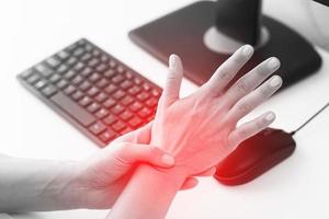 Woman working in office with a carpal tunnel syndrome or wrist joint inflammation photo