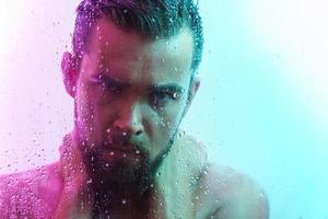 Portrait of handsome young man captured through wet glass in colorful light photo
